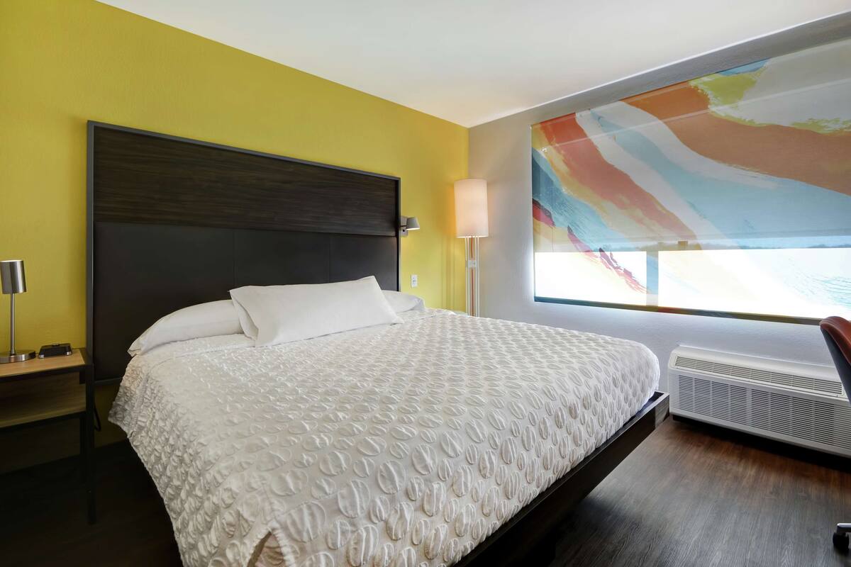 Habitación de hotel con una cama grande, una mesita de noche, una lámpara y una ventana con vistas.