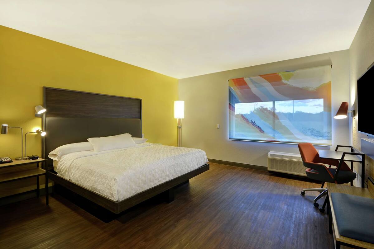 Habitación de hotel con cama, lámparas de noche, escritorio, silla y un ventanal con vistas.