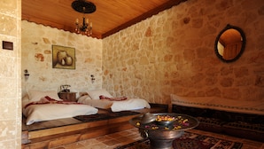 A room with a stone wall, a bed with white linens, a wooden floor, a metal basin with flowers, and a mirror on the wall. - Likya Yolu Palas (Demre)
