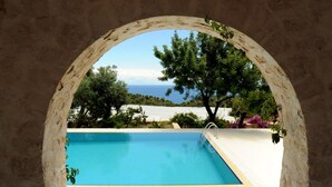 An outdoor swimming pool with a view of the sea, framed by a stone archway. - Likya Yolu Palas (Demre)