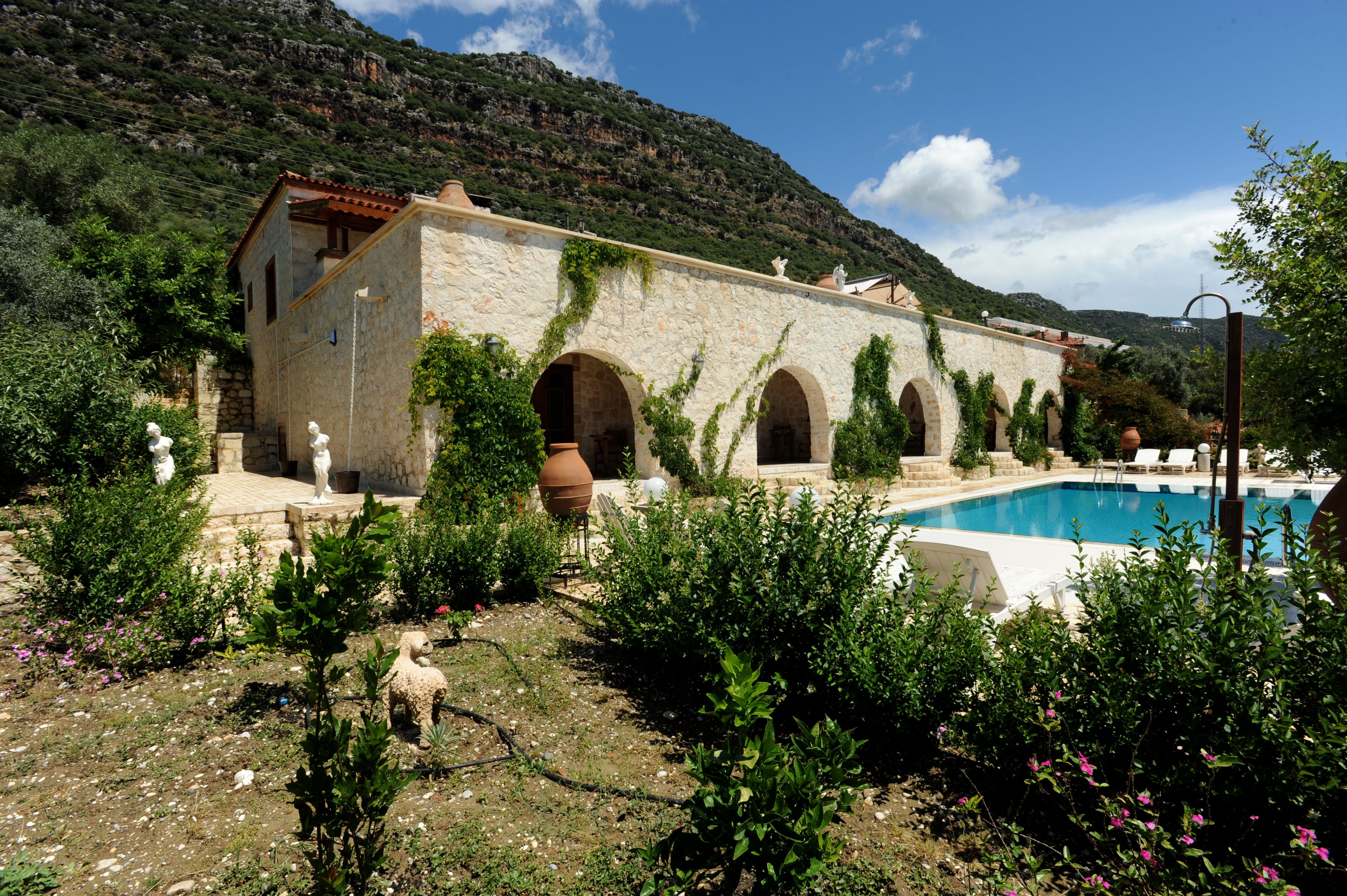 Un edificio de piedra con arcos, una piscina y montañas al fondo.