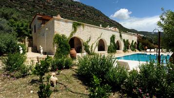 Un edificio de piedra con arcos, una piscina y montañas al fondo.