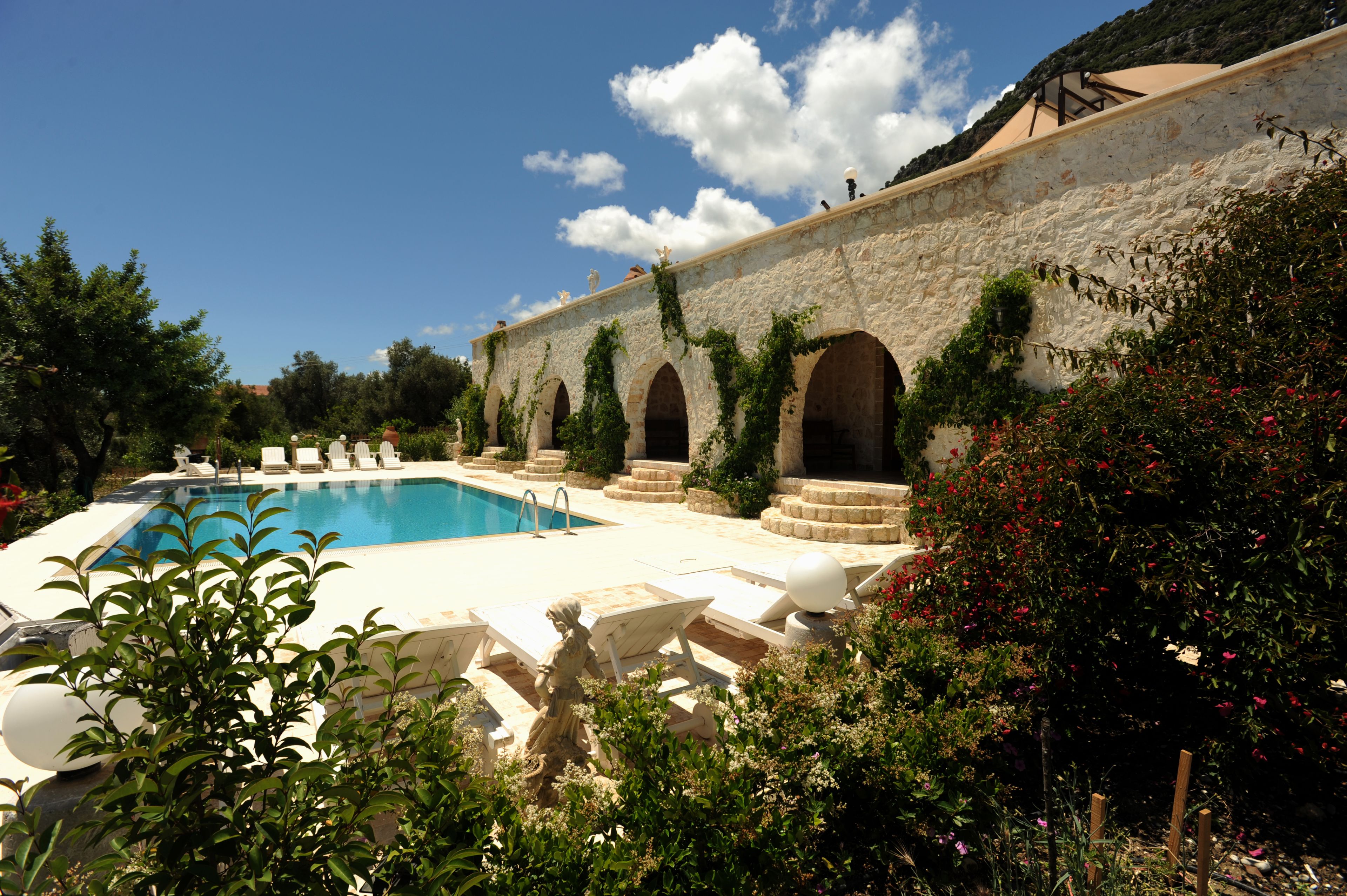 Zona de piscina con muro de piedra, arcos y una estatua.