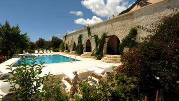 Zona de piscina con muro de piedra, arcos y una estatua.