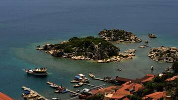 Un pueblo costero con islas rocosas, un muelle con barcos y edificios tradicionales con tejados rojos.