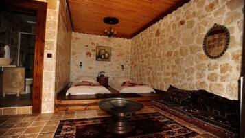 Una habitación con paredes de piedra, techo de madera, una cama con almohadas, una mesita pequeña y un tapete estampado.