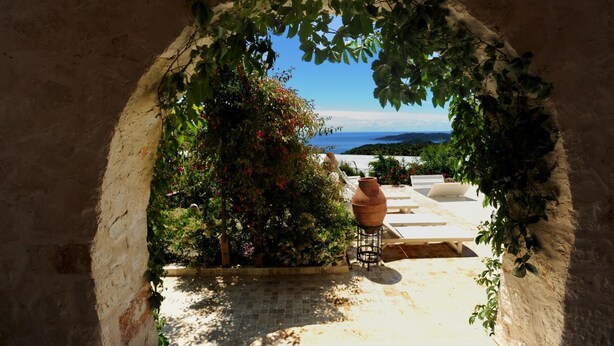 An arched doorway leading to a patio with a view of the sea, surrounded by greenery and a terracotta pot. - Likya Yolu Palas (Demre)