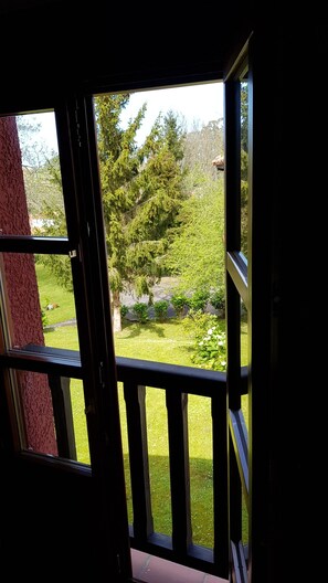 Une vue depuis un balcon doté d’une balustrade, donnant sur un jardin où l’on peut admirer différentes plantes et arbres.