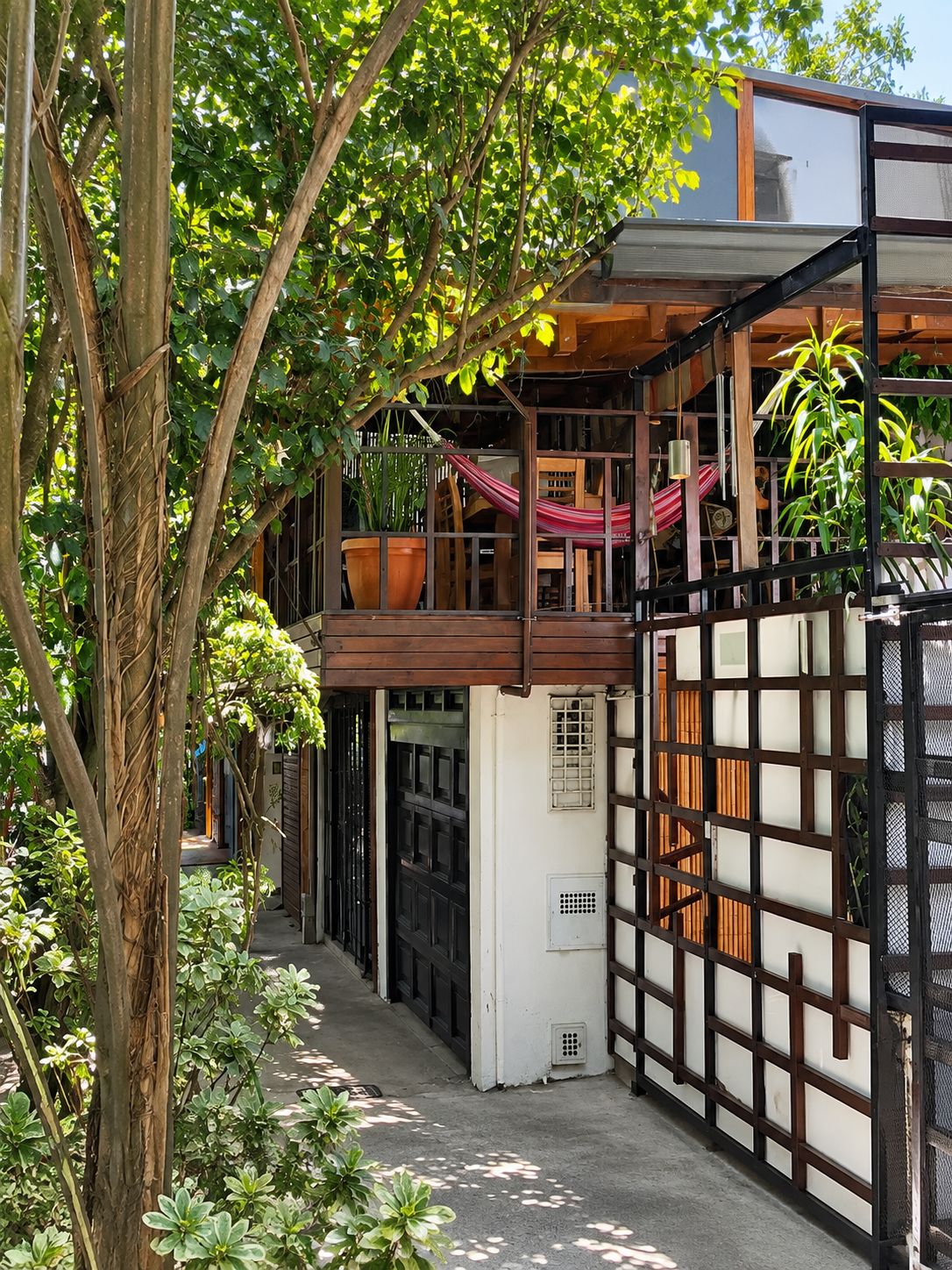 A traditional Japanese-style building with a wooden exterior, a balcony with a hammock, and a large potted plant.
