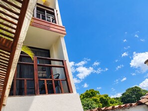Un edificio con balcón, una ventana que ofrece vistas al cielo y una vista parcial de un árbol.