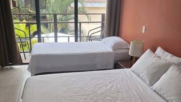 Habitación de hotel con dos camas, un balcón con vistas a zonas verdes y una ventana con cortinas.