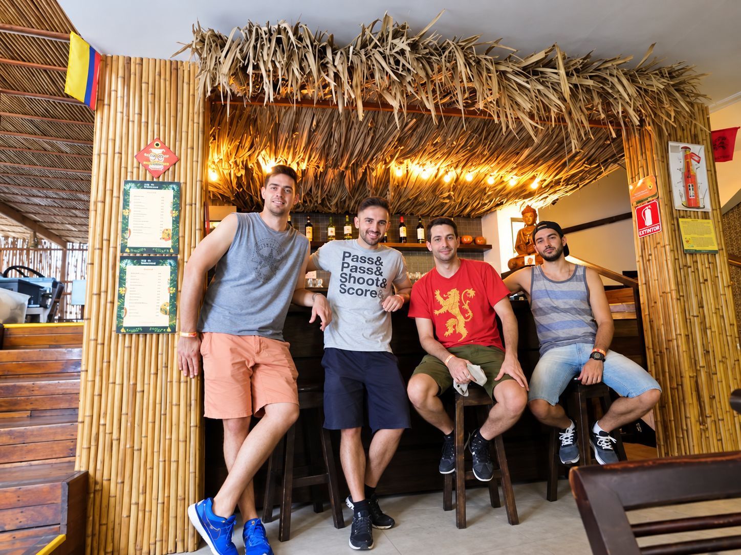Un grupo de personas sentadas en una habitación con paredes de bambú y techo de paja.