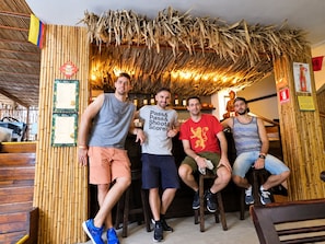 Un grupo de personas sentadas en una habitación con paredes de bambú y techo de paja.