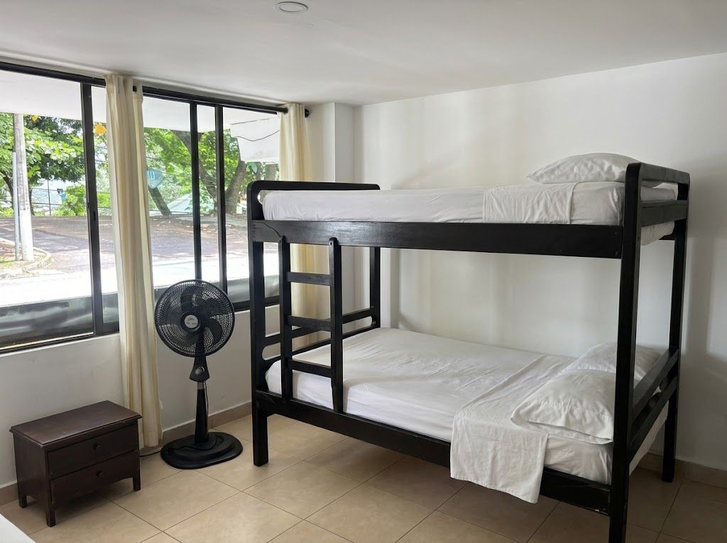 Una cama litera con un ventilador y una mesita de noche en una habitación con ventana.
