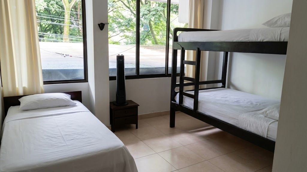 A room with two single beds, a bunk bed, a heater, and a window with a view of the street.