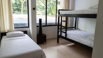 A room with two single beds, a bunk bed, a heater, and a window with a view of the street.