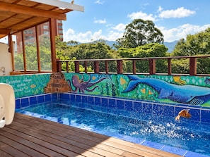 Una piscina con un mural de vida marina, rodeada por una terraza de madera y vistas a zonas verdes y edificios.