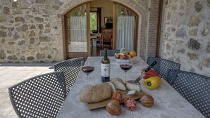 An outdoor dining area with stone walls, a table set with bread, tomatoes, a bottle of Chianti, and wine glasses. - Antica Fonte Resort (Casole d'Elsa)