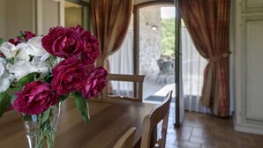 A dining area with a wooden table and chairs, a vase of flowers, and a view through a glass door to an outdoor patio. - Antica Fonte Resort (Casole d'Elsa)