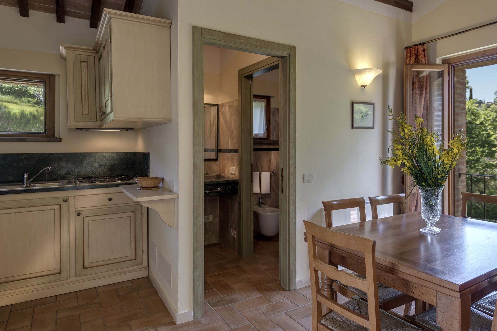 Una cocina con armarios de madera, una mesa de comedor con sillas y un florero con flores.