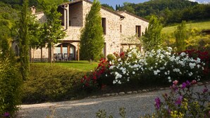 A stone building with a garden in front, surrounded by greenery and hills. - Antica Fonte Resort (Casole d'Elsa)