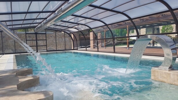 An indoor swimming pool with a glass ceiling, stone walls, and a central water feature. - Antica Fonte Resort (Casole d'Elsa)