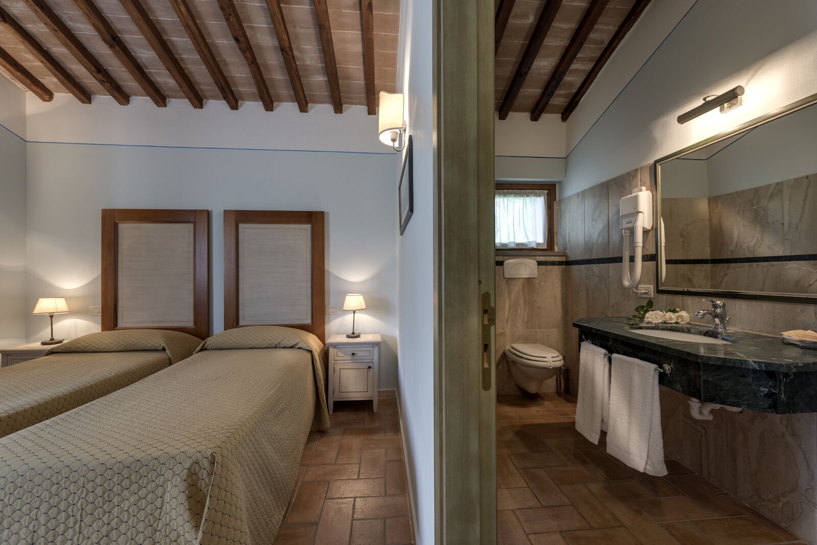A hotel room with two beds, a bathroom with a marble sink, and wooden ceiling beams.