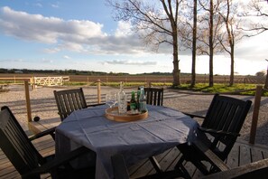 Un área de comedor al aire libre con una mesa para dos, rodeada de sillas y una bandeja con botellas y vasos.