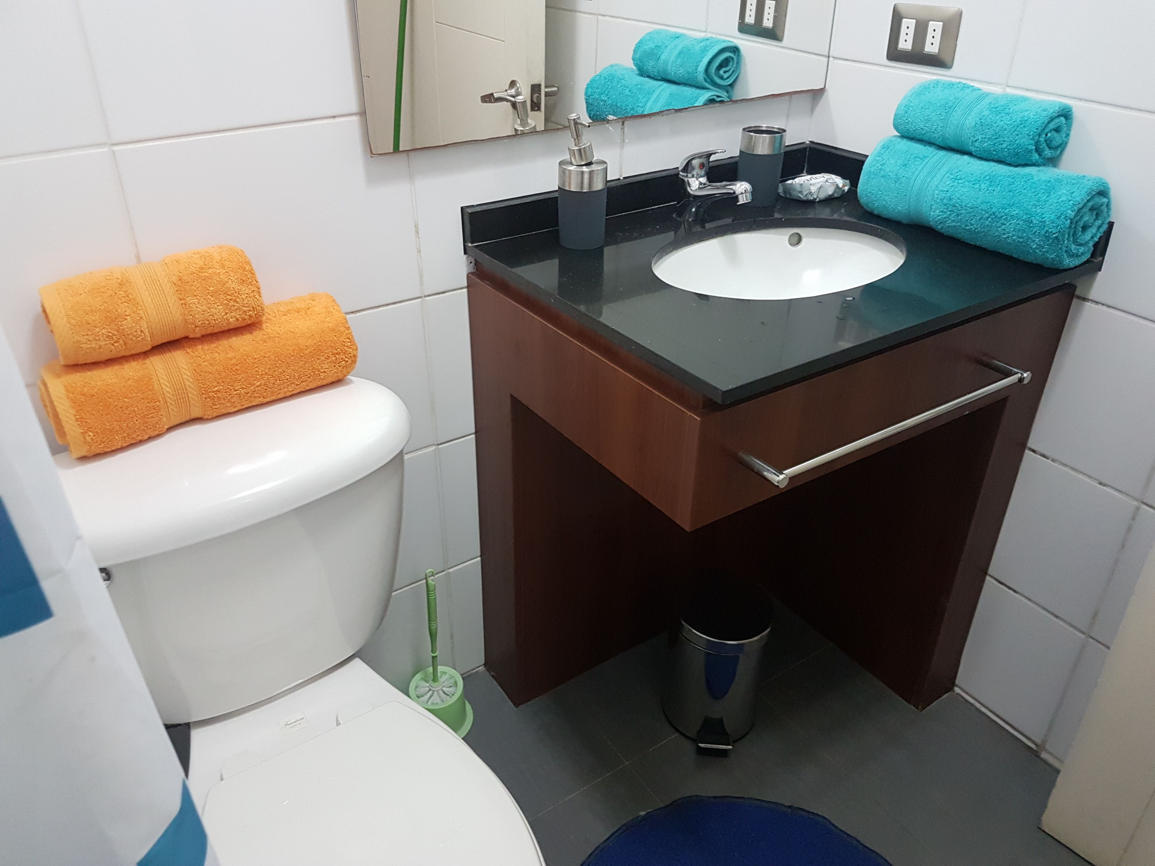 A bathroom with a white toilet, a sink with a black countertop, and two towels (orange and blue) on the sink.