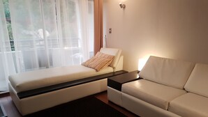 A modern living room with a sofa, a small bed, a coffee table, and a large window with sheer curtains. - Apart Reñaca C-206 (Vina del Mar)