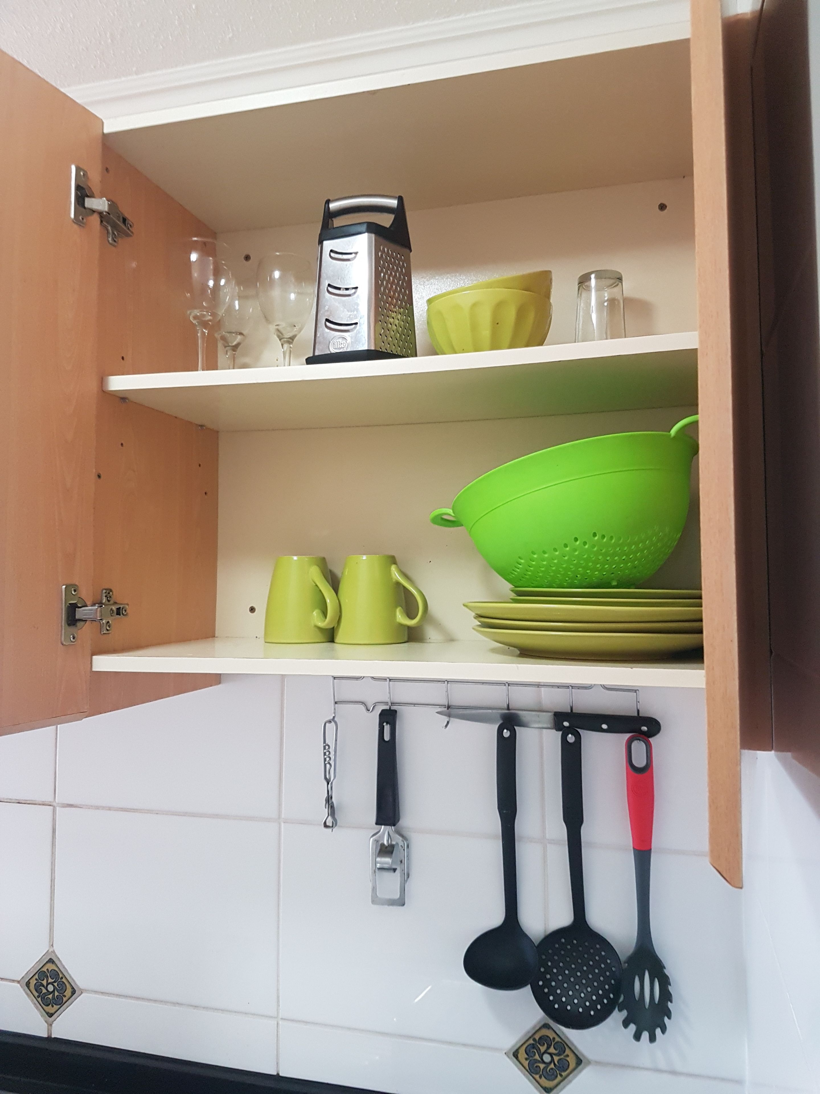 Una cocina con armarios blancos, un colgador para utensilios y una estantería con vajilla verde y amarilla.