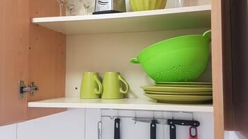 Una cocina con armarios blancos, un colgador para utensilios y una estantería con vajilla verde y amarilla.