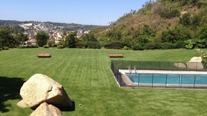 A backyard with a swimming pool, a lawn, and a view of a town in the distance. - Apart Reñaca C-206 (Vina del Mar)