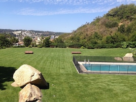 A backyard with a swimming pool, a lawn, and a view of a town in the distance.