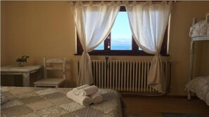 Ein Schlafzimmer mit Bett, Stuhl, Tisch und einem fenster mit Vorhängen.