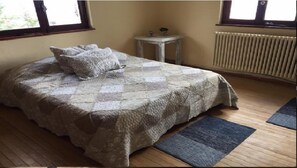 Ein Schlafzimmer mit gesteppter Bettdecke, einem kleinen Nachttisch mit Lampe und einem Heizkörper.