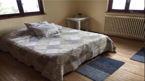 Un dormitorio con colcha acolchada, una mesita de noche con lámpara y un radiador.
