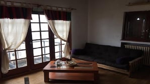Una sala de estar con un sofá de color oscuro, una mesa de centro de madera y una ventana con cortinas.