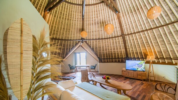 Un interior acogedor con techo de paja, zona de comedor, sofá y televisor.