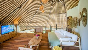 Una habitación amplia con techo inclinado, suelo de madera, un sofá, un televisor y una mesa de comedor con un cuenco de fruta.