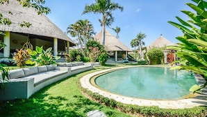 Un resort con bungalows de techo de paja, una piscina central y abundante vegetación.