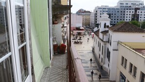 A narrow street with buildings on either side, a tiled plaza in the center, and a few people walking.