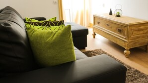 A modern living room with a black leather sofa, green cushions, a wooden dresser, and a glass vase on top.