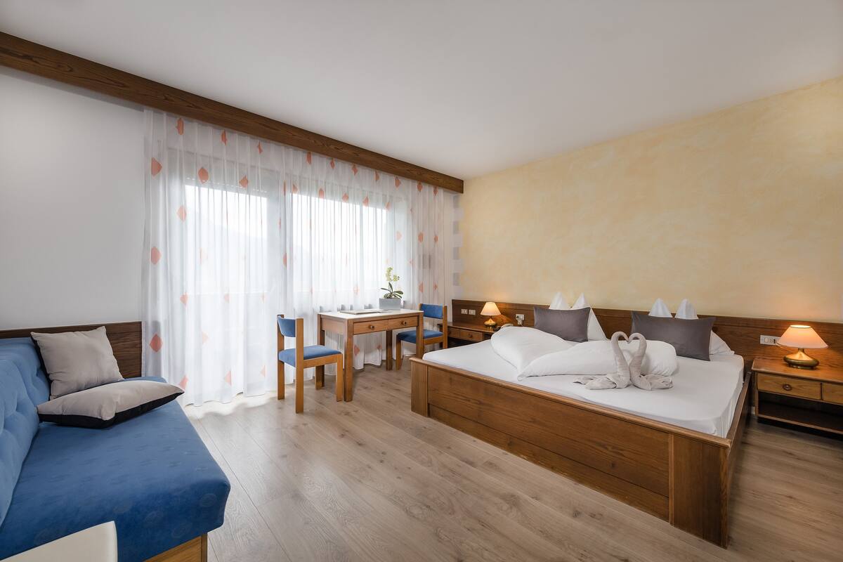A hotel room with a bed, a desk, a chair, and a small table.