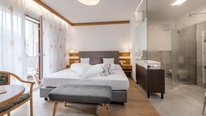 A modern bedroom with a large bed, bedside tables, a bench, a desk, and a shower area. - Hotel Wilma (Nalles)