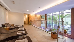 A spa area with reclining chairs, a marble wall, and a glass railing overlooking a garden. - Hotel Wilma (Nalles)