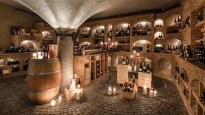 A wine cellar with stone walls, wooden barrels, and shelves filled with wine bottles. - Hotel Wilma (Nalles)
