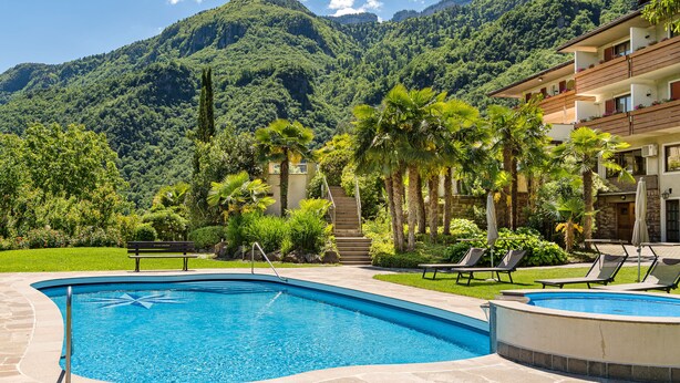 A pool area with a view of mountains, a staircase leading to a building, and lounge chairs. - Hotel Wilma (Nalles)
