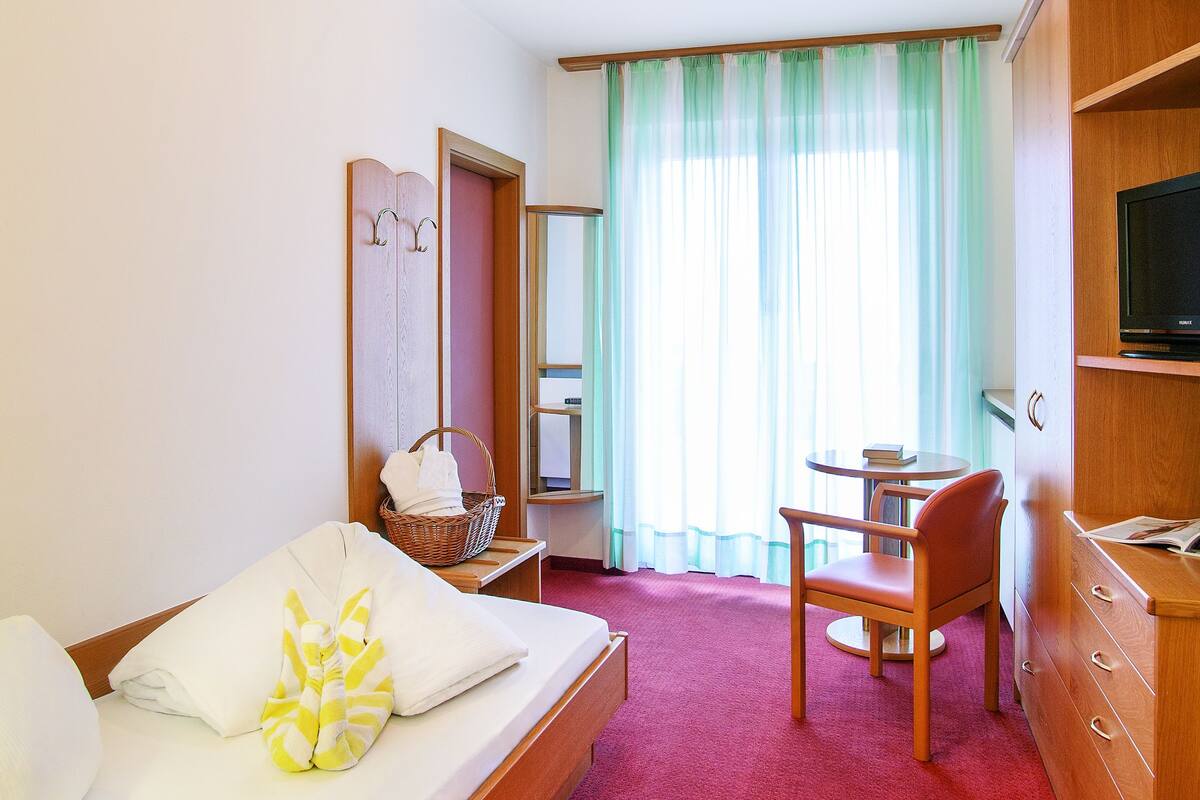 A hotel room with a bed, a desk, a chair, a TV, and a wardrobe.