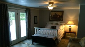 A bedroom with a bed, a nightstand with a lamp, a ceiling fan, and a view through a glass door. - Open All Year. Ausable River Access. Newly Remodeled! (Roscommon)